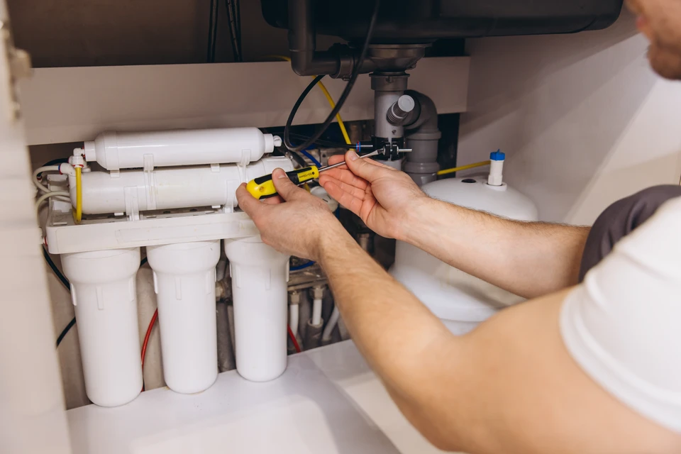 Un plombier en polo blanc travaille accroupi dans un local technique, intervenant sur un système de chauffage