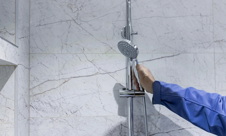Plombier professionnel installant un système de douche dans une salle de bain carrelée grise